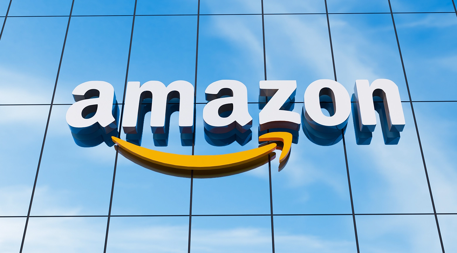 Logotipo tridimensional de Amazon sobre una fachada de vidrio reflejando el cielo azul.