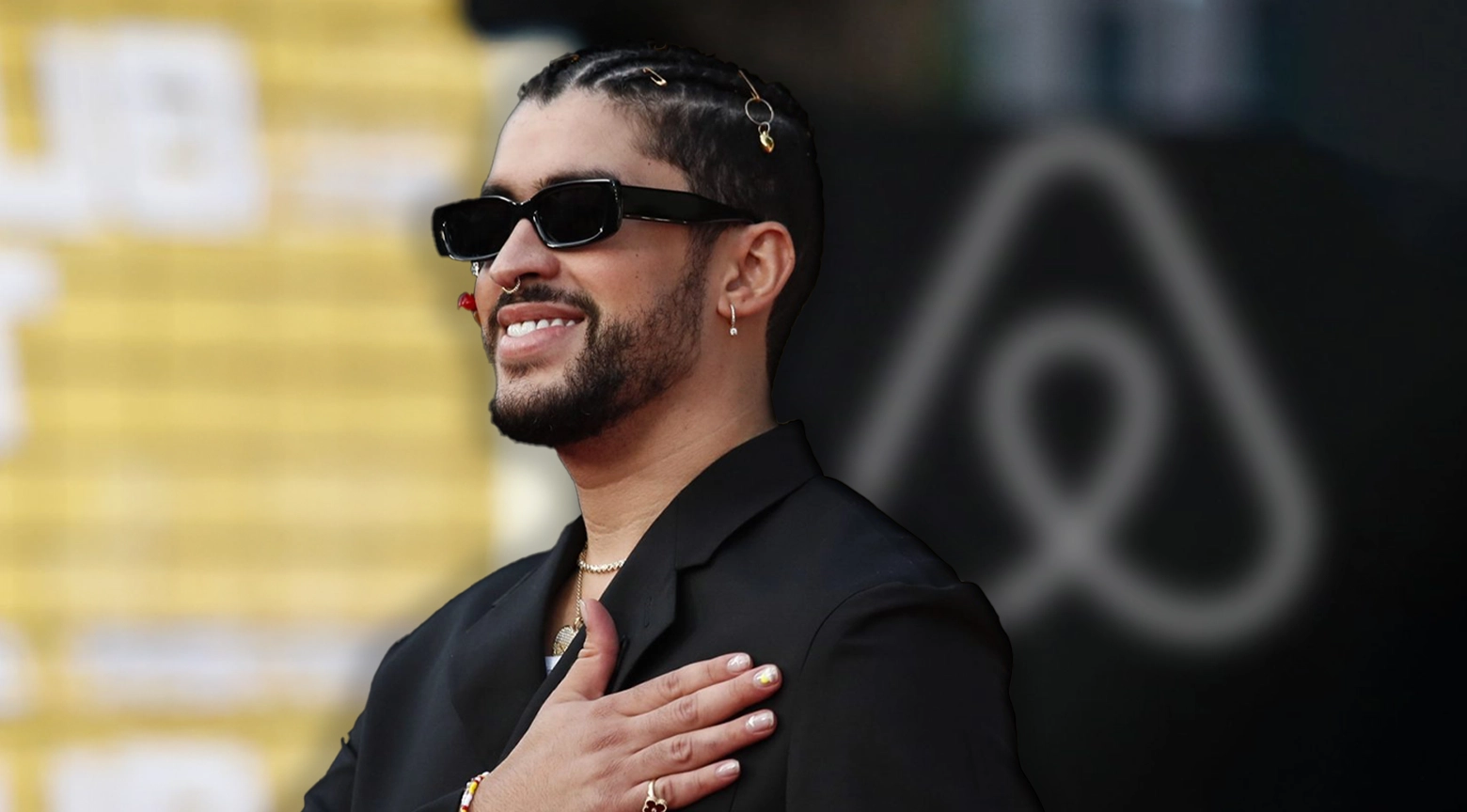 Artista urbano sonriente con gafas oscuras y traje negro durante un evento de Airbnb en Puerto Rico.