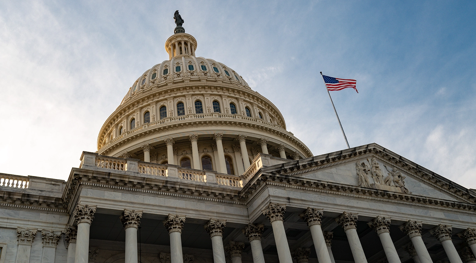 Fachada del Capitolio de los Estados Unidos con la bandera estadounidense ondeando en lo alto.