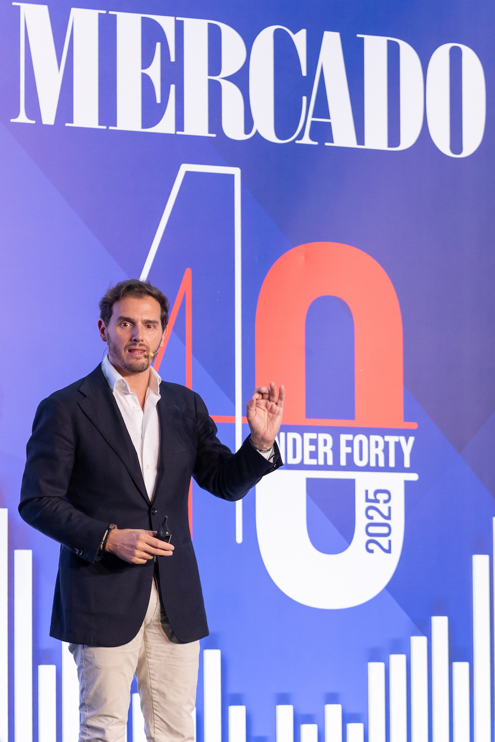 hombre de traje en un escenario dictando una conferencia con una pantalla de fondo y la palabra aprendizaje