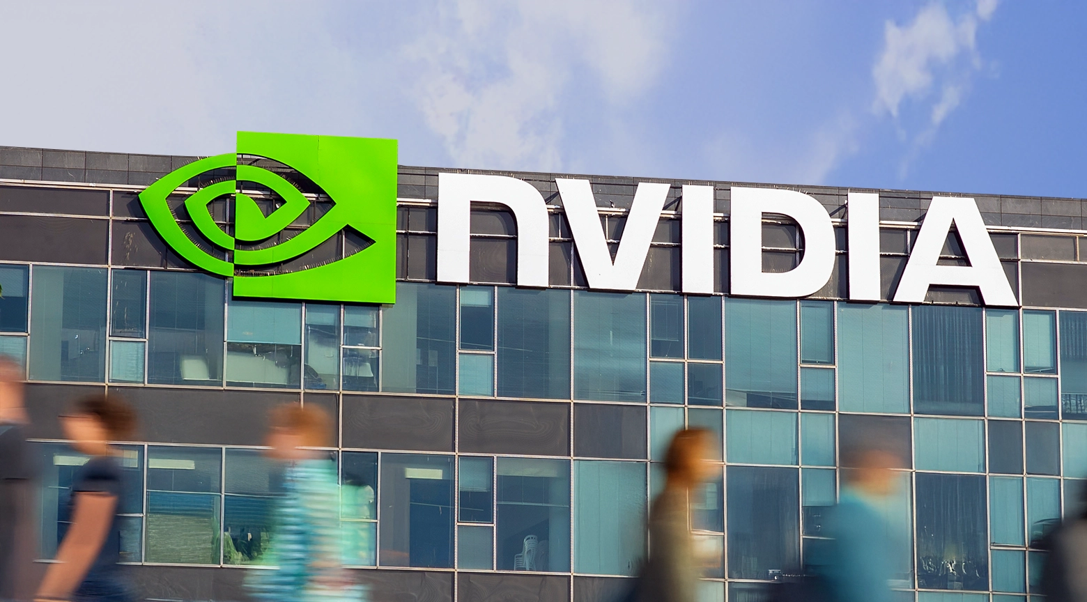 Logotipo de Nvidia en la fachada de un edificio moderno con ventanales de vidrio y fondo de cielo nublado.