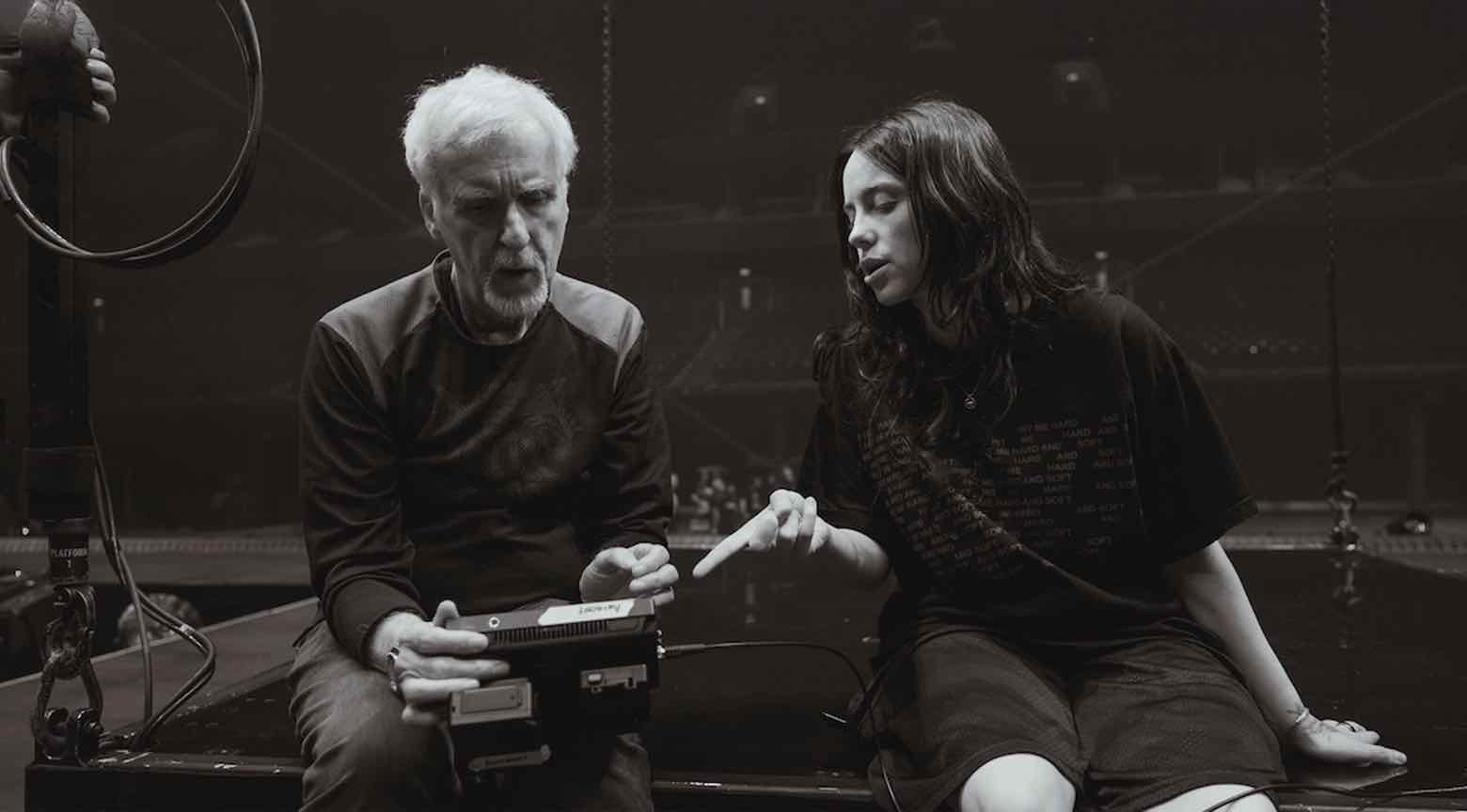 Billie Eilish y James Cameron discutiendo el contenido de un documental mientras se encuentran en un espacio de trabajo. La imagen es en blanco y negro, con ambos sentados y mirando una pantalla mientras intercambian ideas.