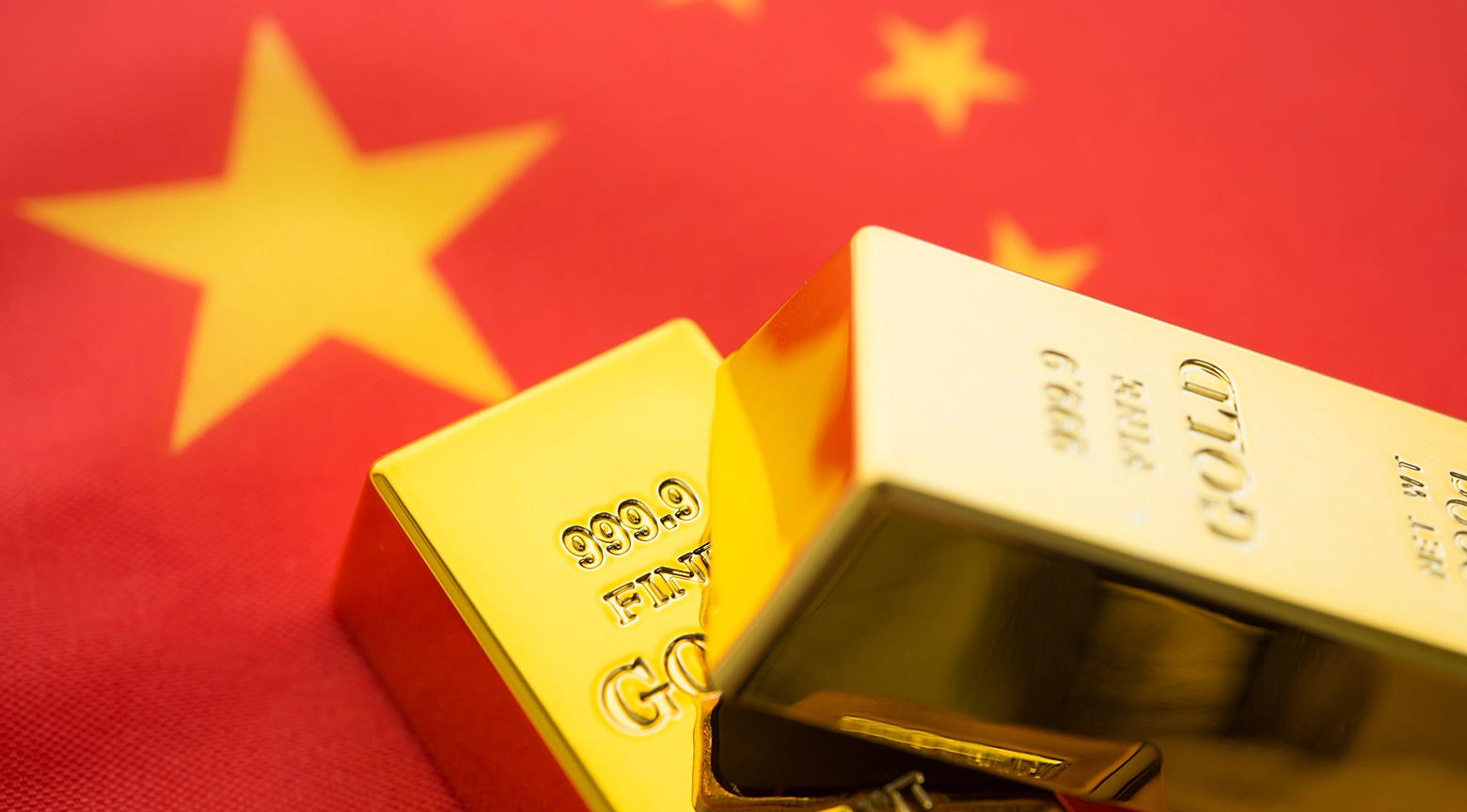 Lingotes de oro sobre una bandera de China, simbolizando la fortaleza del oro frente a las políticas económicas del país.
