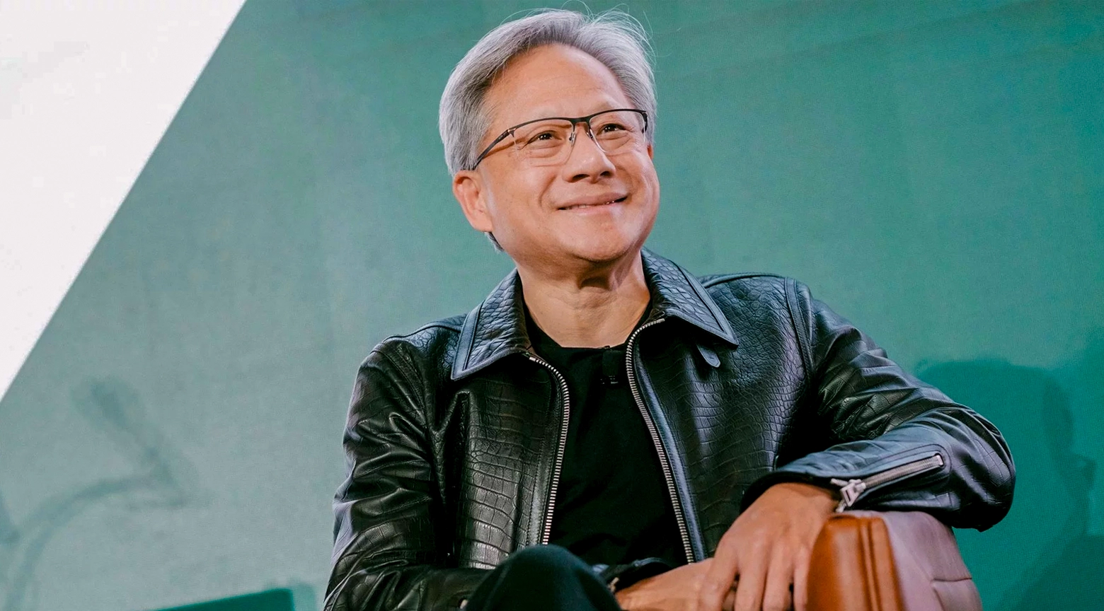 Ejecutivo de tecnología con chaqueta de cuero negro sonriendo durante una conferencia, sobre un fondo verde.