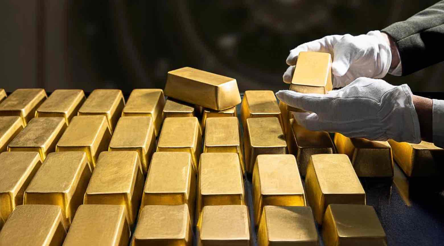 Lingotes de oro siendo manipulados por un trabajador con guantes blancos en una bóveda.