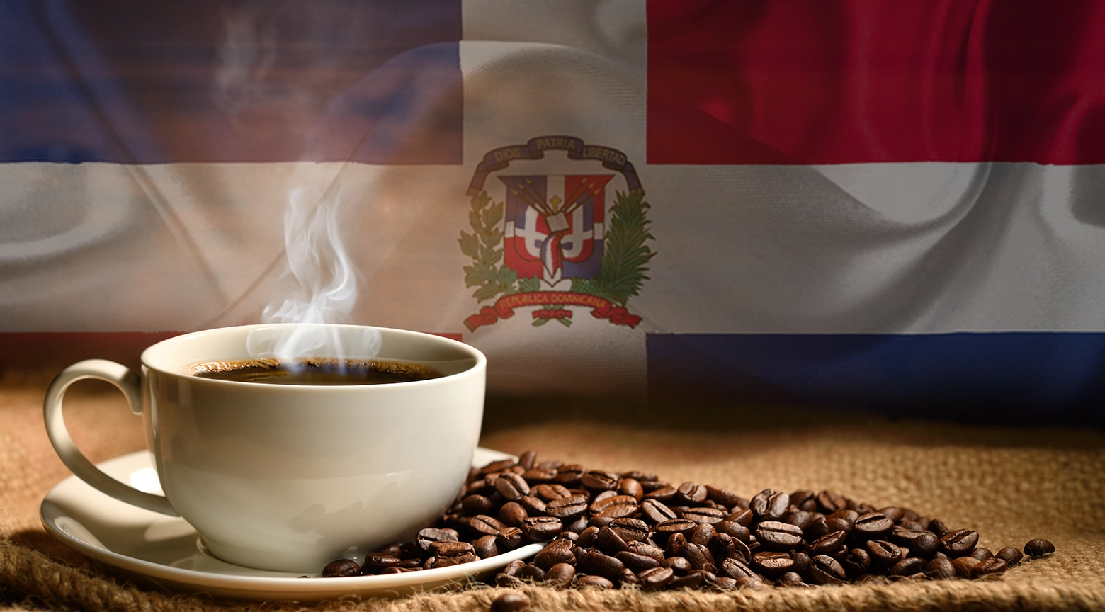 Taza de café caliente junto a granos de café sobre una mesa rústica, con la bandera de la República Dominicana de fondo.