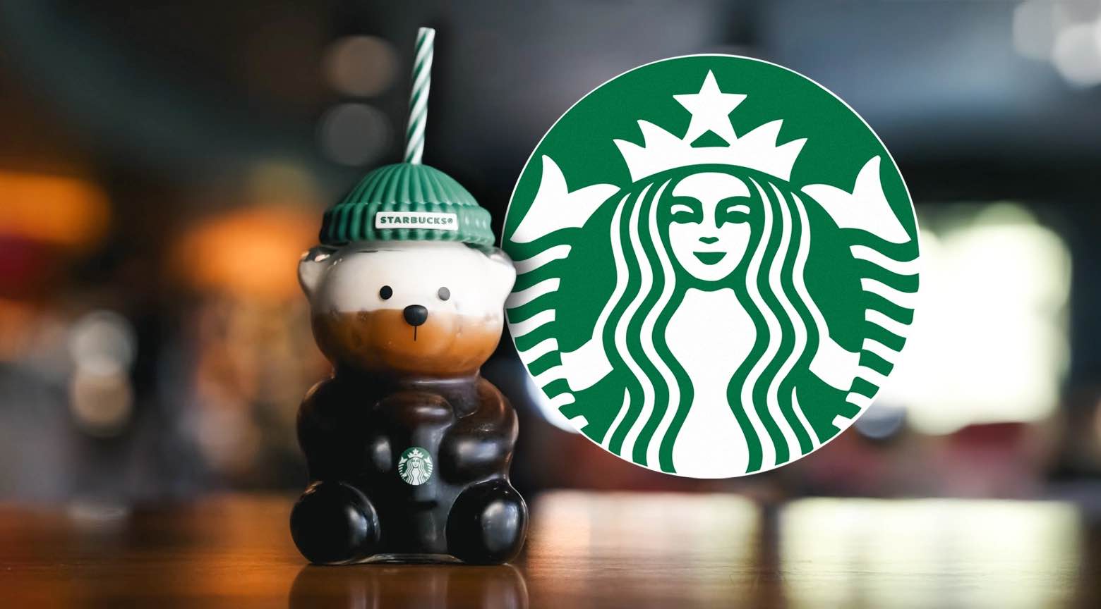 Botella en forma de oso con diseño de Starbucks sobre una mesa, acompañada del logotipo verde de la marca en un fondo desenfocado.