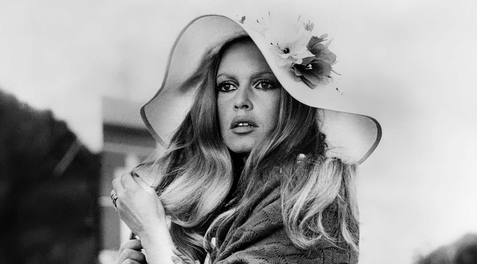 Mujer con sombrero de ala ancha y flor decorativa posa para una fotografía en blanco y negro, con expresión serena y mirada directa.