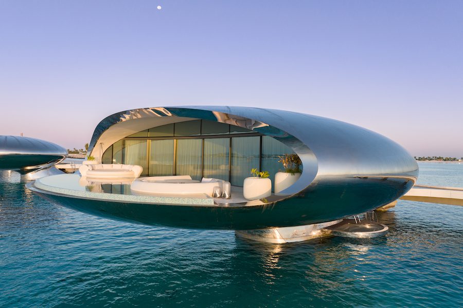 Villa de lujo de diseño futurista sobre el agua, con estructura curva metálica, piscina privada y amplios ventanales frente al mar.