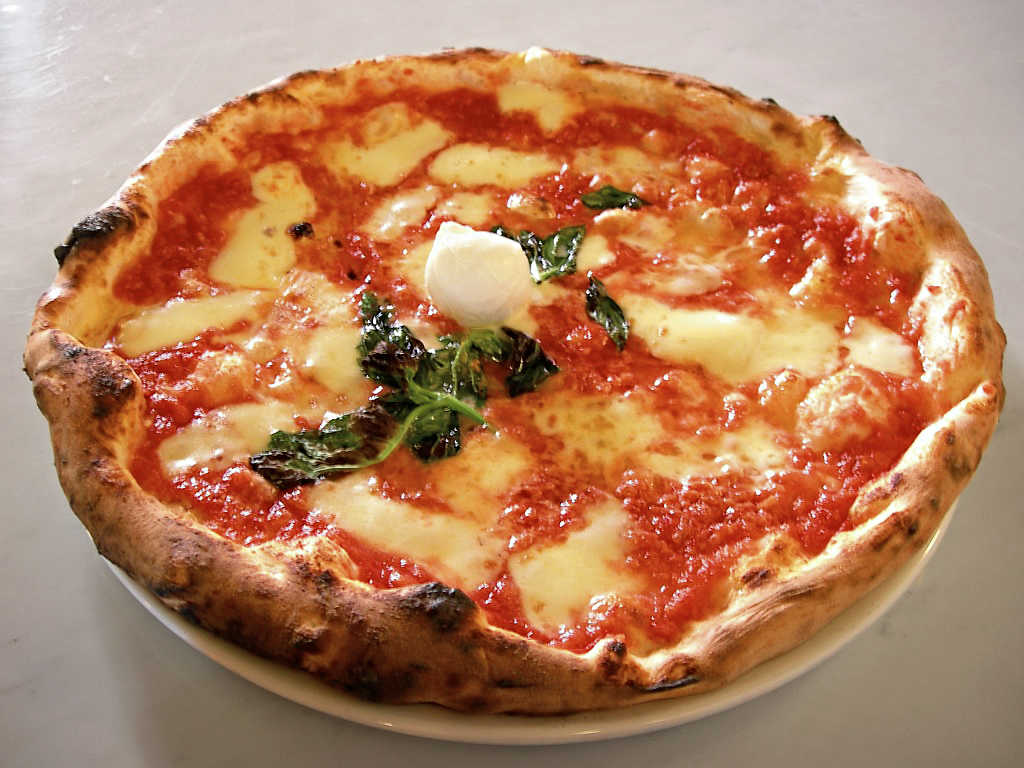 Pizza margarita artesanal con salsa de tomate, mozzarella derretida, hojas de albahaca fresca y borde dorado ligeramente tostado.
