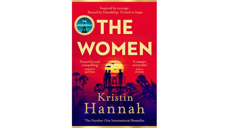Portada del libro The Women de Kristin Hannah, con una ilustración de dos mujeres sobre una pasarela al atardecer, en tonos rojos y azules, evocando camaradería y resiliencia.