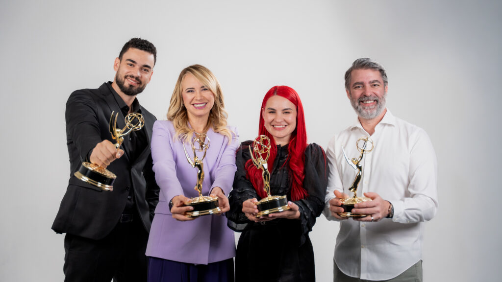 Cuatro personas posan sonrientes frente a un fondo neutro, sosteniendo estatuillas Emmy doradas extendidas hacia la cámara.