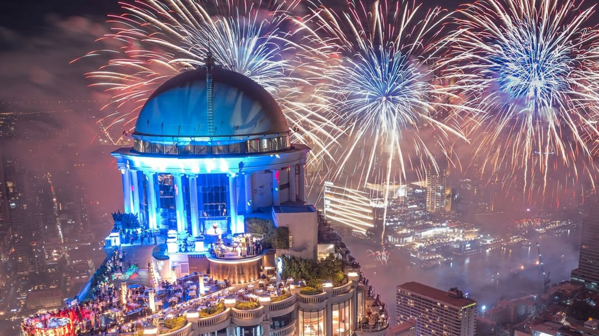 Fuegos artificiales iluminan el cielo nocturno sobre un edificio emblemático durante la celebración de Año Nuevo en una gran ciudad.