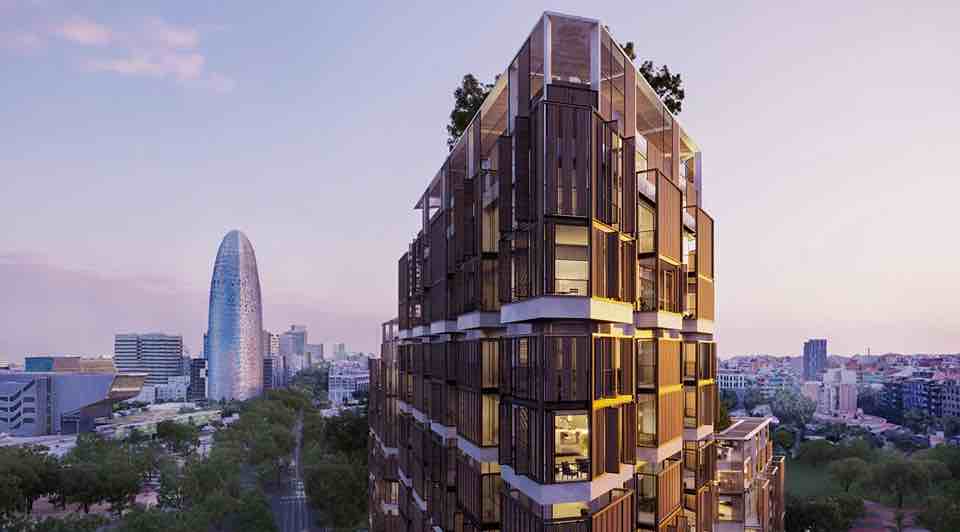 Vista de un moderno barrio de lujo en Barcelona, con un edificio elegante y contemporáneo en primer plano, y la famosa Torre Agbar al fondo.