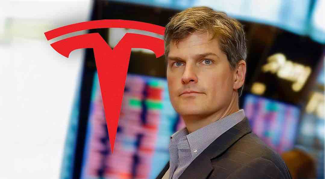 Retrato de un hombre frente al logo de Tesla con pantallas bursátiles de fondo.