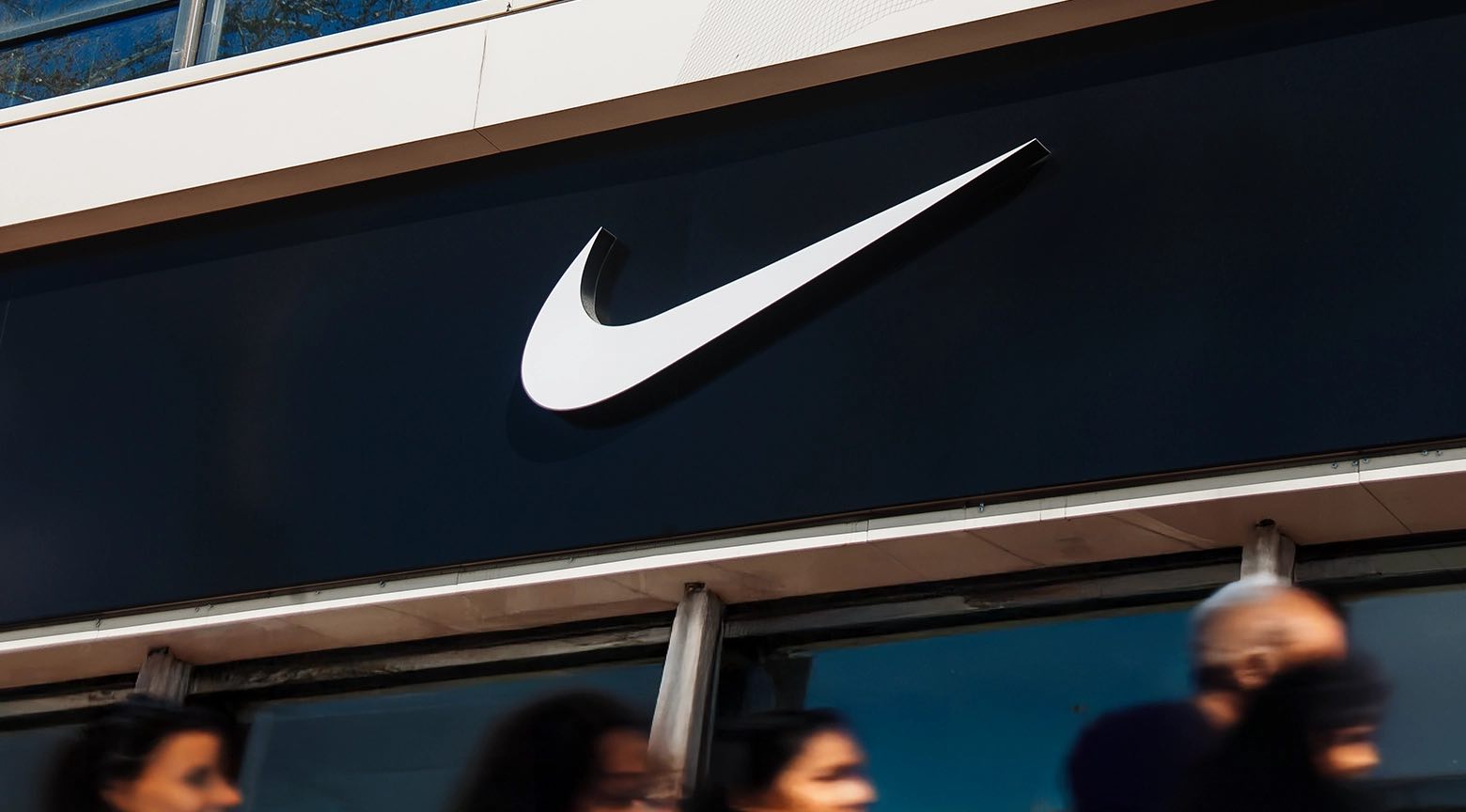 Fachada de una tienda Nike con el logotipo de la marca sobre fondo negro y personas caminando frente al local.