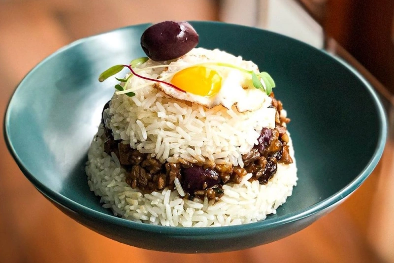 Arroz tapado servido en un plato hondo, con capas de arroz blanco y guiso de carne, coronado con un huevo frito y una aceituna.