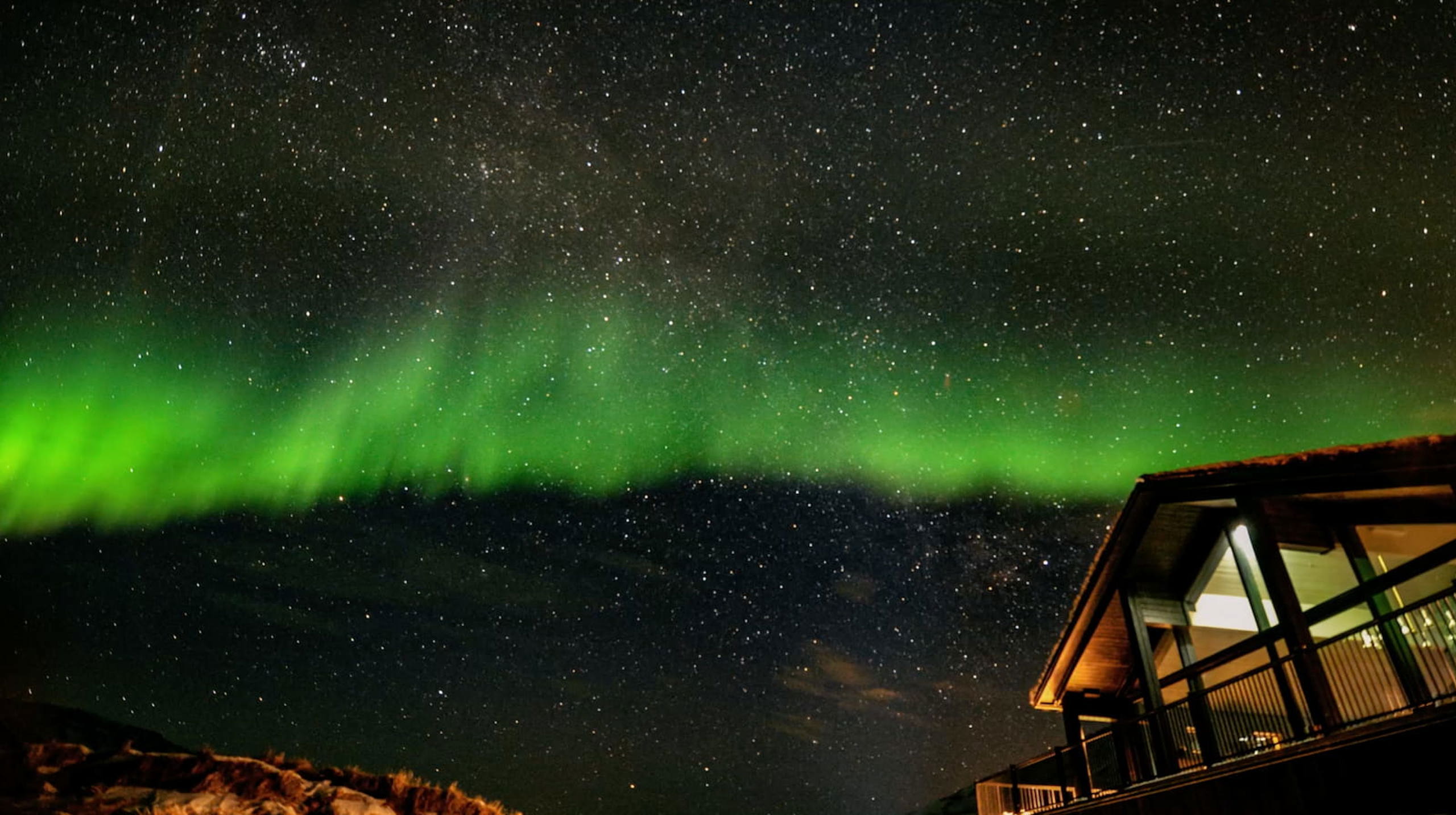 Aurora boreal verde ilumina el cielo estrellado sobre una cabaña moderna en un paisaje invernal.