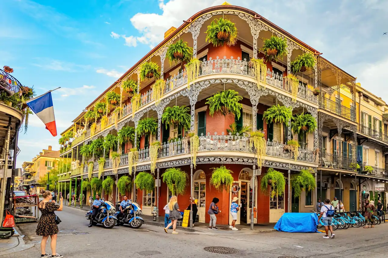 Edificio histórico de Nueva Orleans con balcones de hierro forjado cubiertos de plantas, en una esquina concurrida del Barrio Francés.