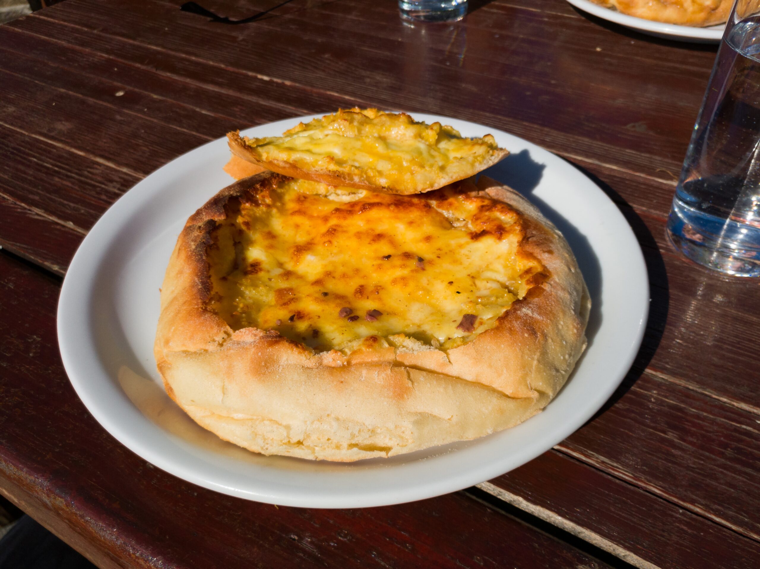 Pan redondo horneado relleno de queso fundido y dorado, servido en un plato blanco sobre una mesa de madera.