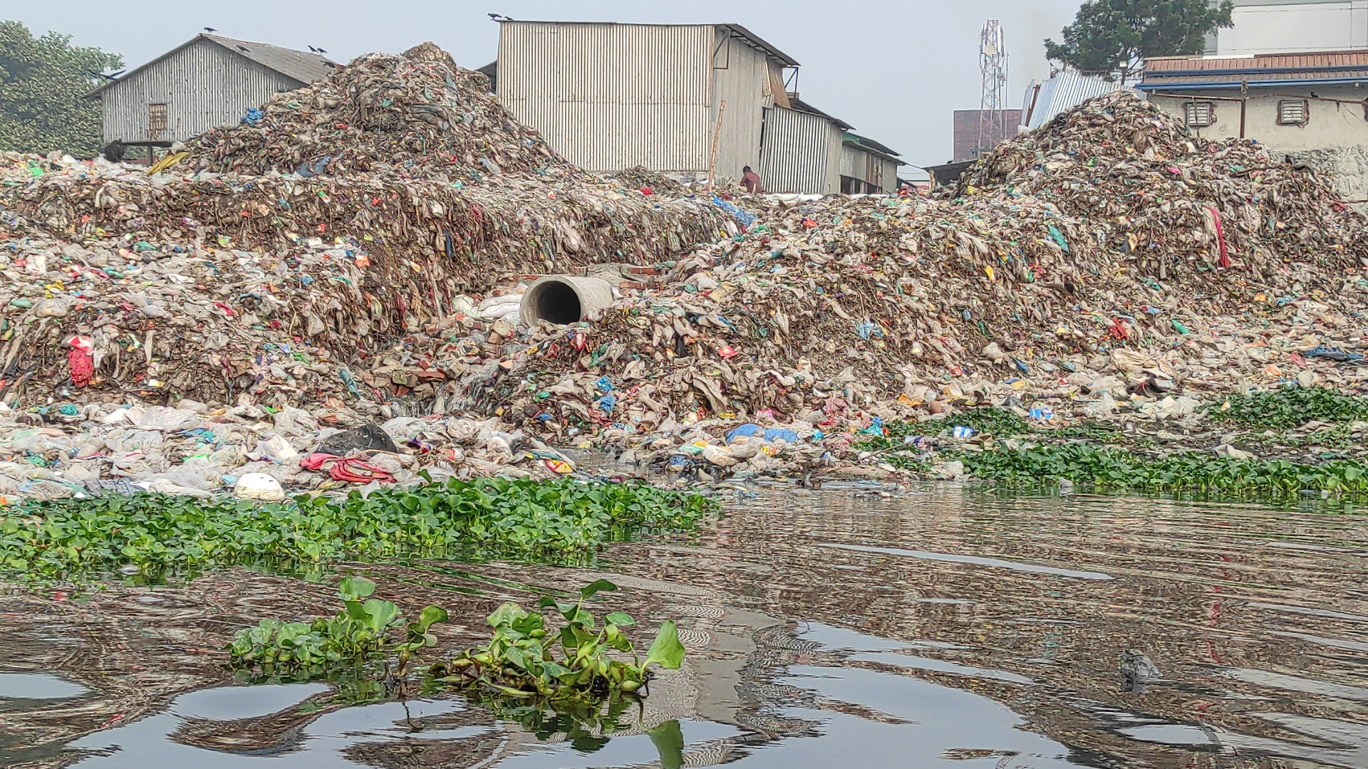 Montículos de residuos sólidos acumulados junto a un cuerpo de agua, evidenciando contaminación ambiental y manejo inadecuado de desechos.