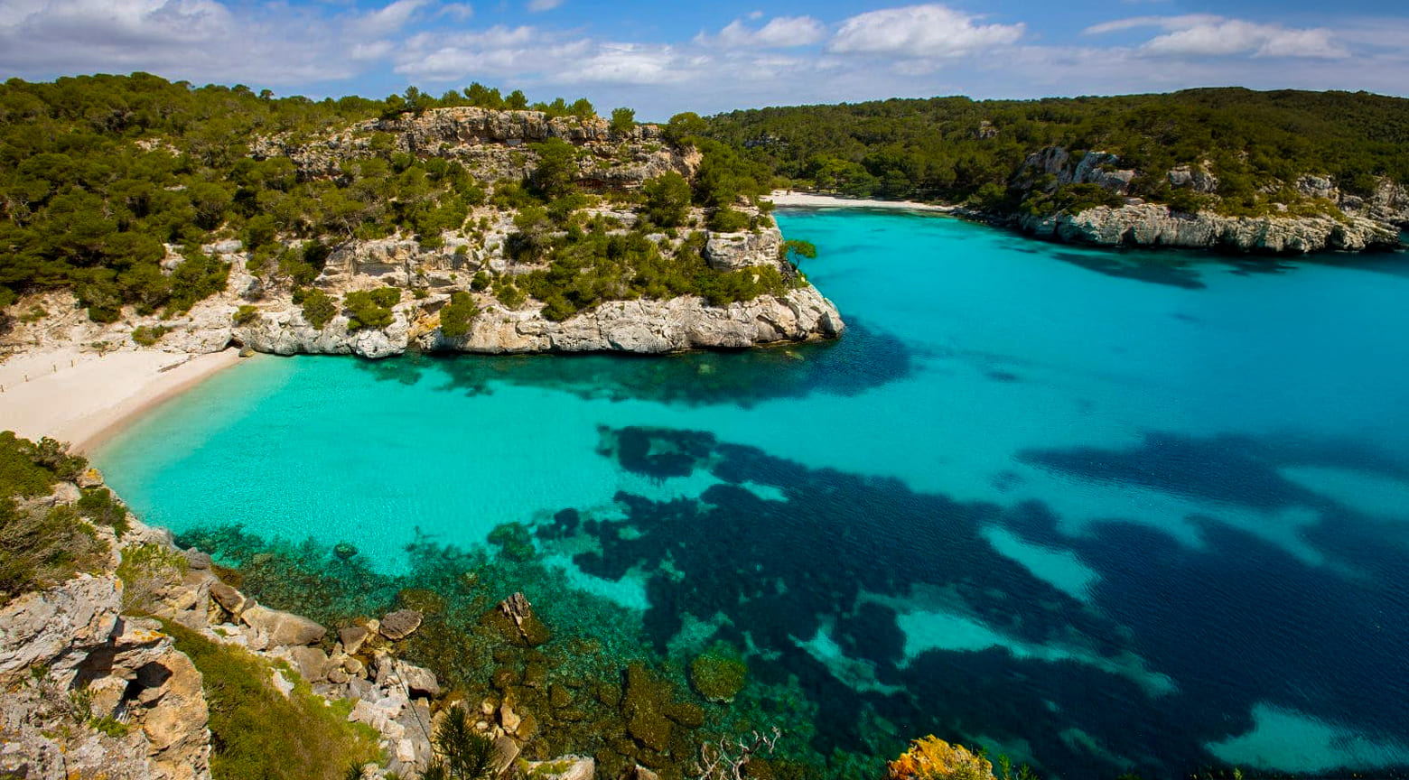 Cala Macarelleta en Menorca con aguas turquesas, acantilados rocosos y una pequeña playa de arena clara.