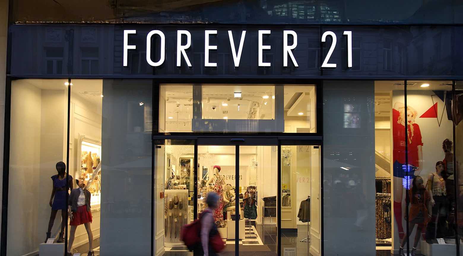 Fachada de una tienda Forever 21 iluminada de noche, con vitrinas y maniquíes visibles en el interior.
