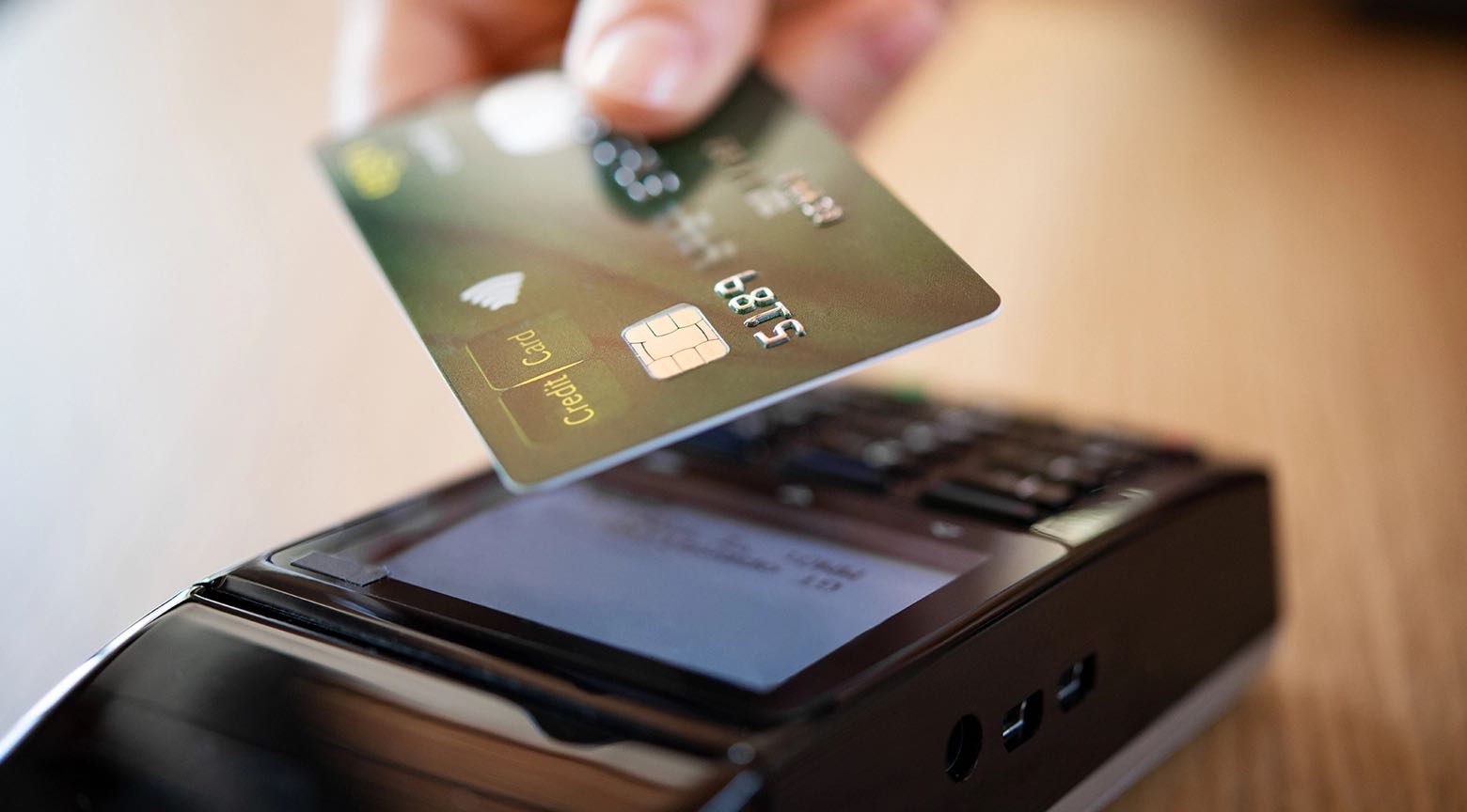 Persona realizando un pago con tarjeta de crédito en un terminal de punto de venta (POS) en un entorno de compras.