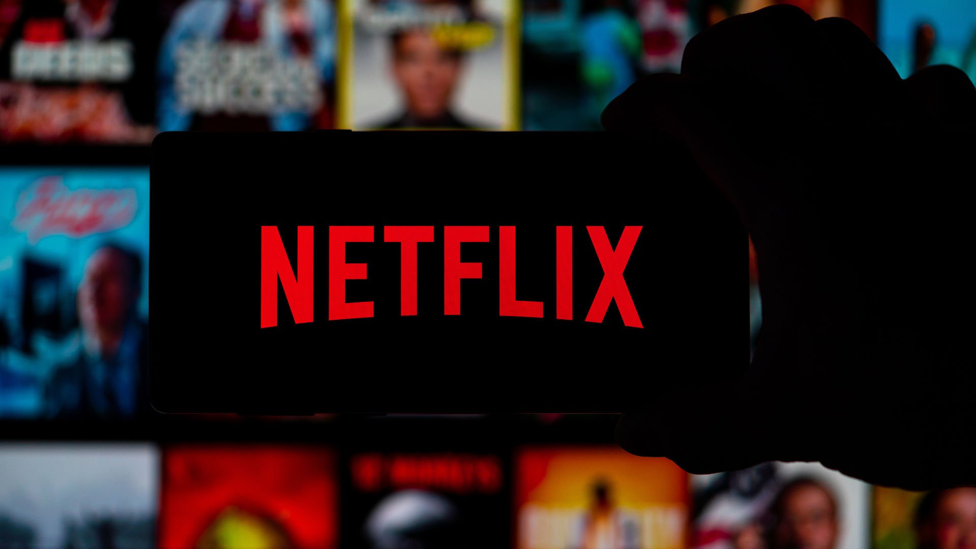 Pantalla de Netflix con su logo rojo al centro y un fondo borroso de series y películas disponibles en la plataforma.