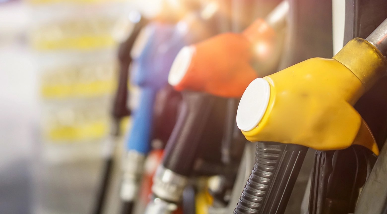 Boquillas de surtidores de gasolina en una estación de servicio, alineadas en distintos colores.