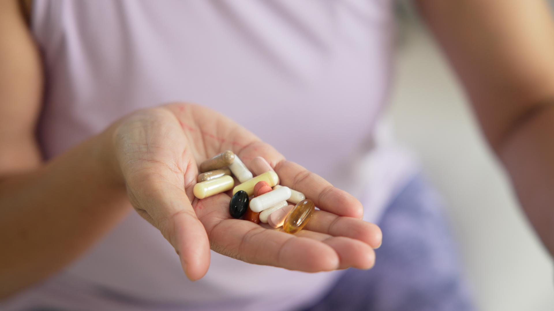 Mano de una mujer sosteniendo varias cápsulas y pastillas de diferentes colores y tamaños.