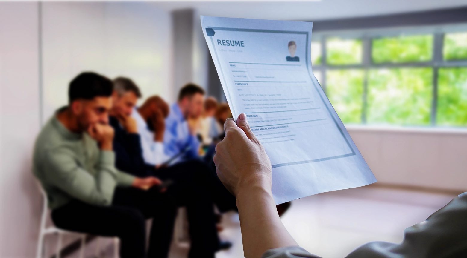 Persona sostiene un currículum mientras varios candidatos esperan sentados en una sala, durante un proceso de selección laboral.