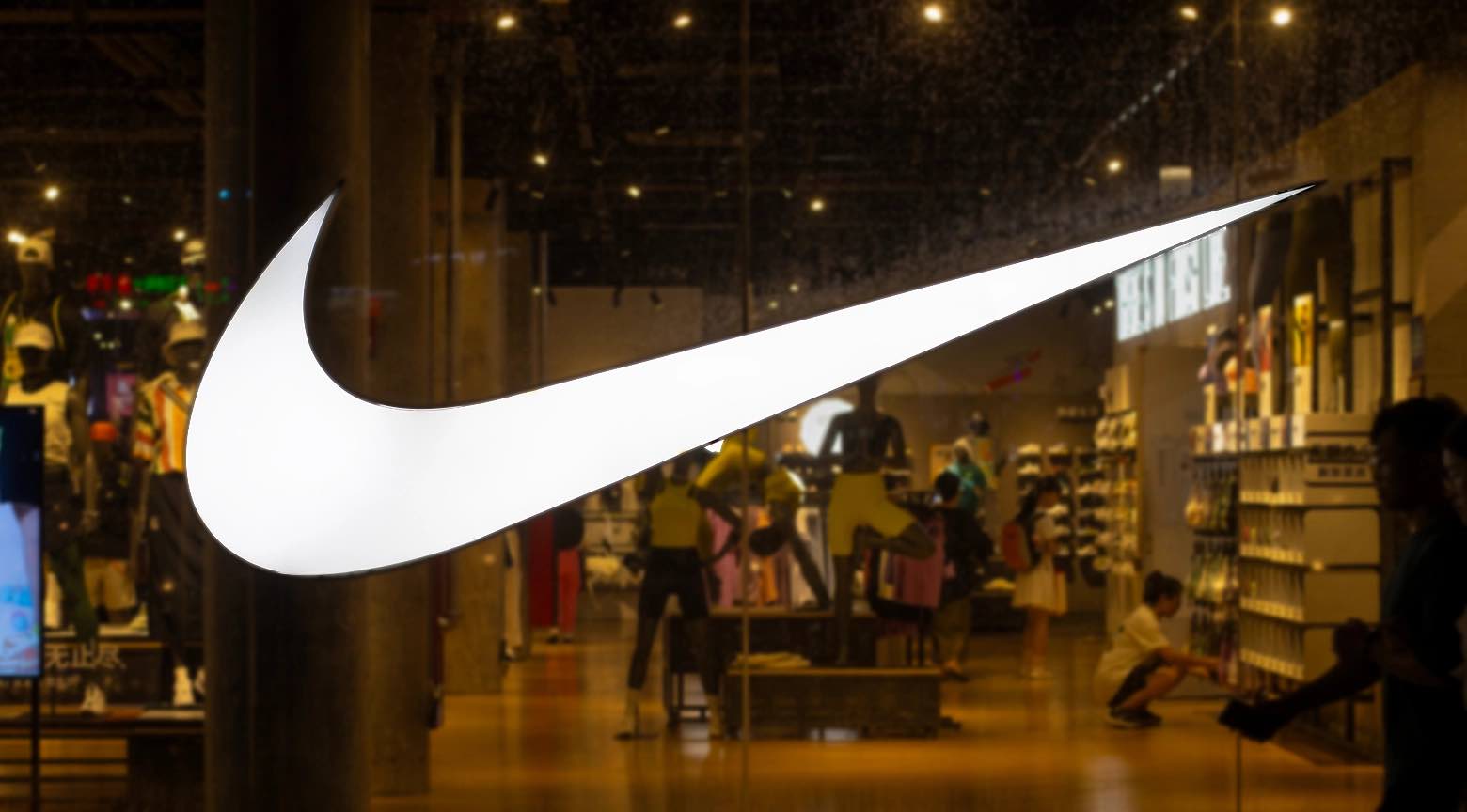 Logo de Nike iluminado en la vitrina de una tienda mientras se observa el interior del local con clientes y productos deportivos.