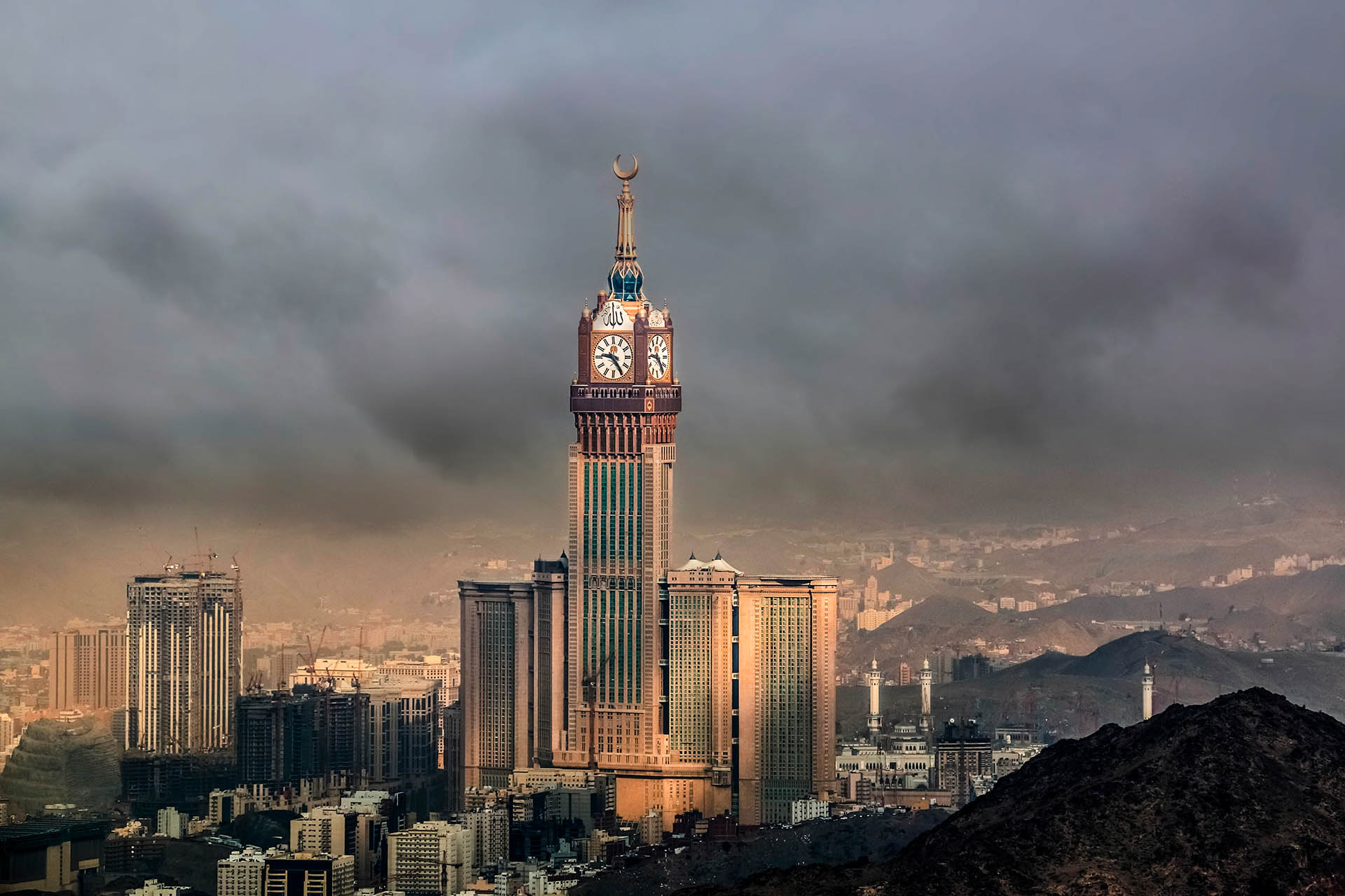 Torre Abraj Al Bait en La Meca, con su icónico reloj coronado por la media luna, dominando el paisaje urbano bajo un cielo nublado.