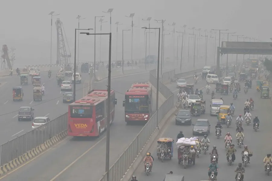 Tráfico vehicular circula bajo una densa capa de smog en una vía urbana, reflejando altos niveles de contaminación del aire.