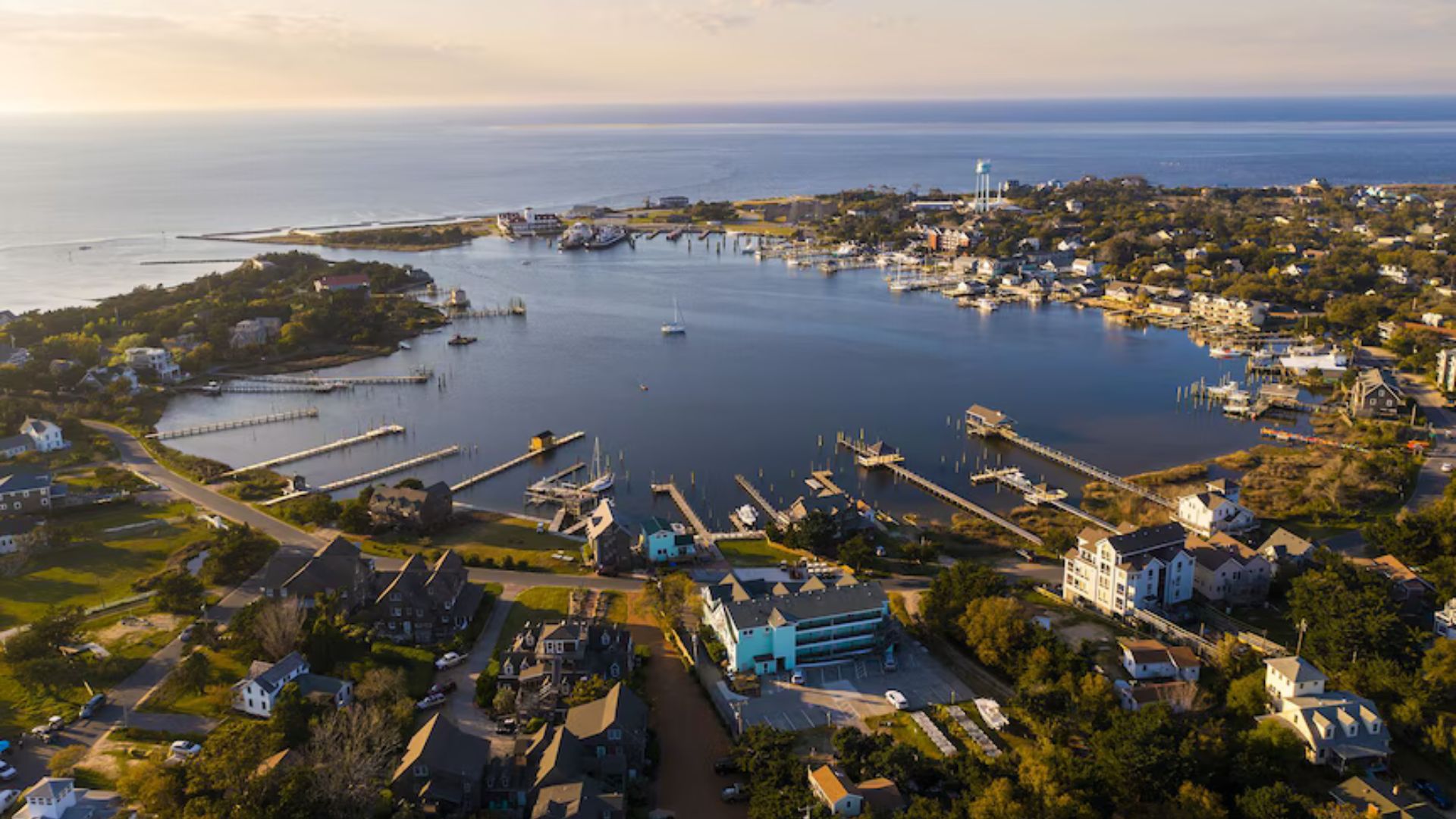 Vista aérea de una bahía con varios muelles y embarcaciones, rodeada de casas y edificios residenciales junto al mar.