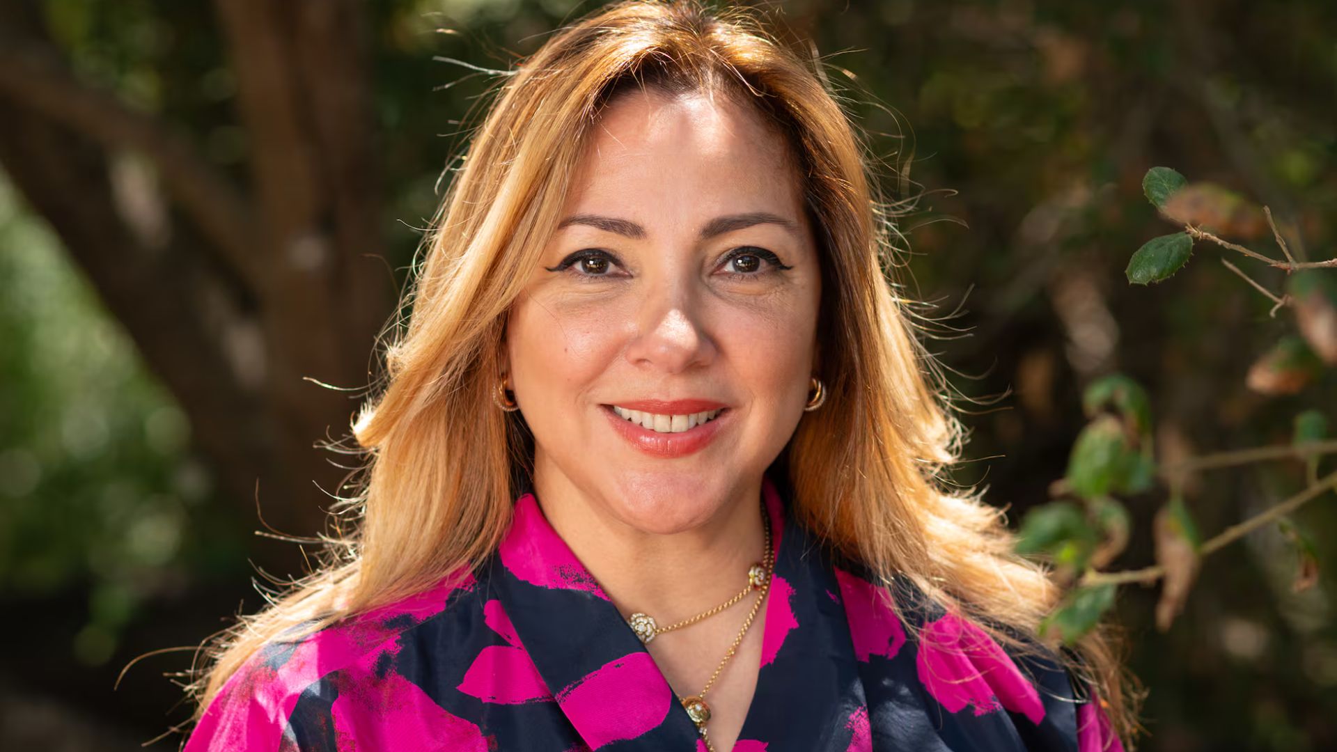 Mujer sonriente al aire libre con blusa de estampado rosa y azul.