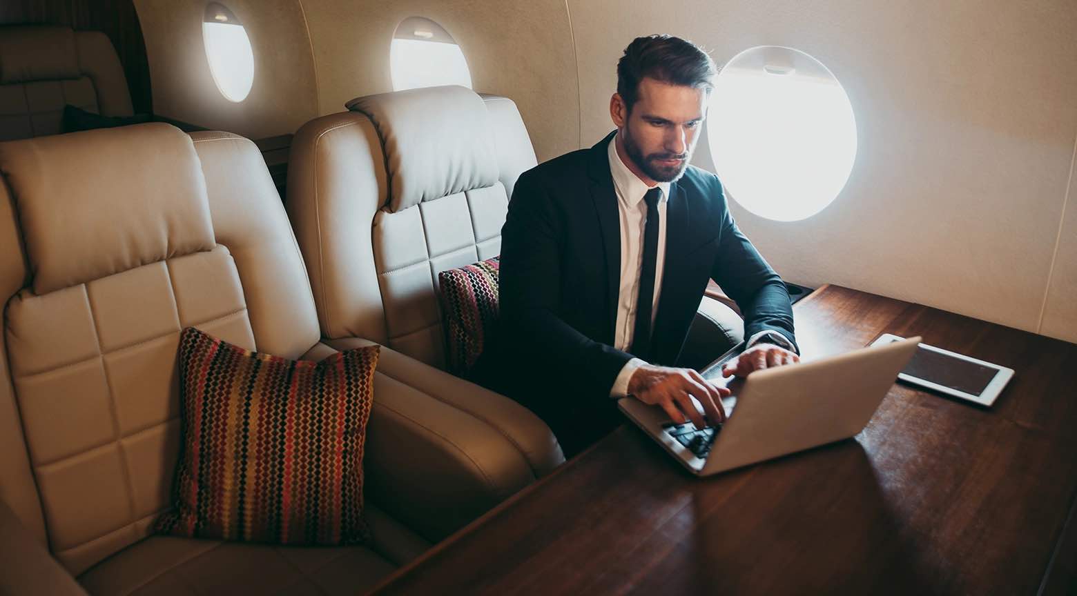 Hombre con traje trabajando en una laptop dentro de un avión privado.