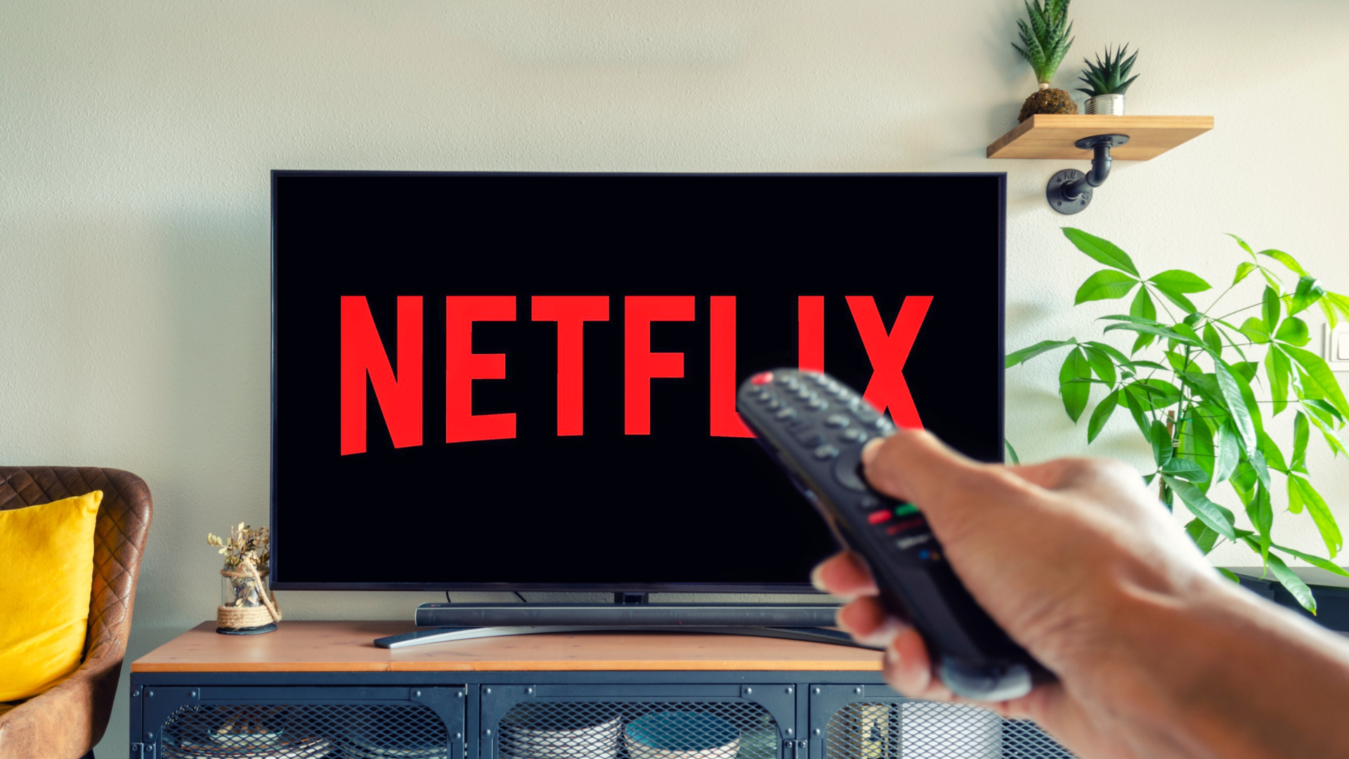 Televisor encendido mostrando el logo de Netflix mientras una persona sostiene un control remoto en una sala de estar.