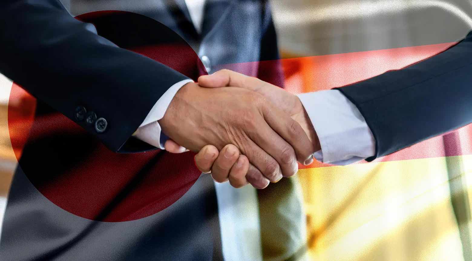 Apretón de manos entre dos ejecutivos con las banderas de Japón y Alemania de fondo.