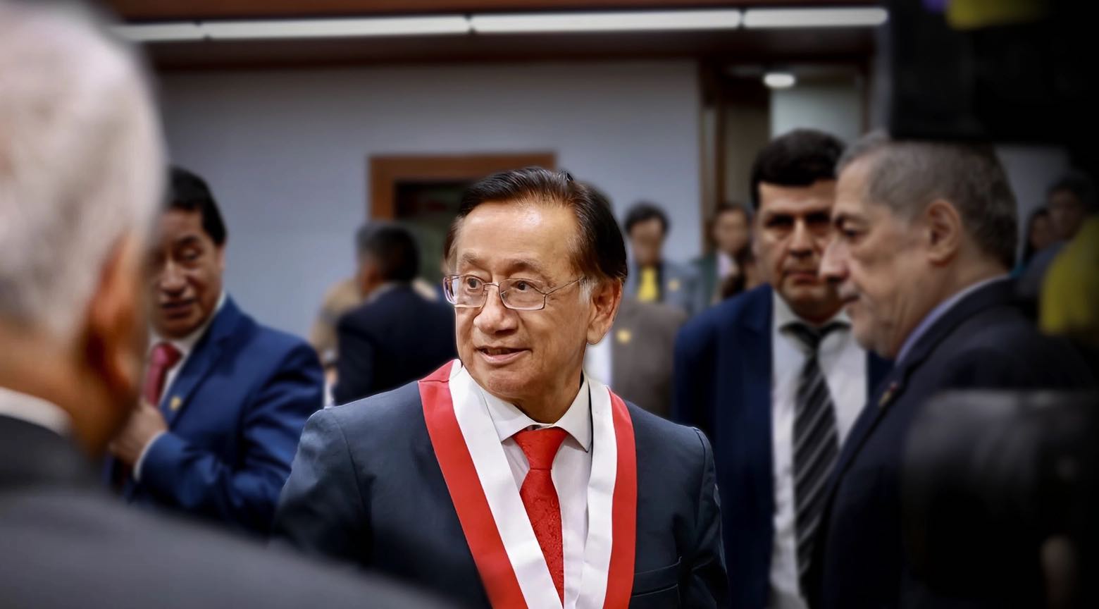 Hombre con banda presidencial roja y blanca conversa con otras autoridades en un acto oficial.