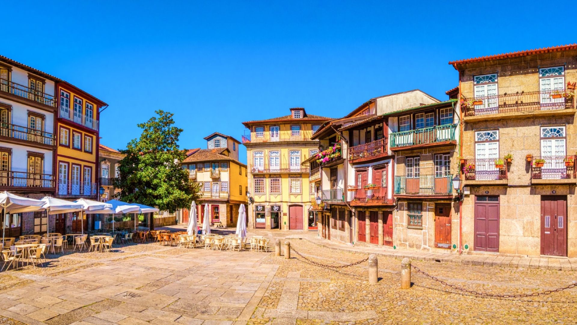 Plaza histórica con edificios coloridos, balcones de madera y terrazas al aire libre bajo cielo despejado.