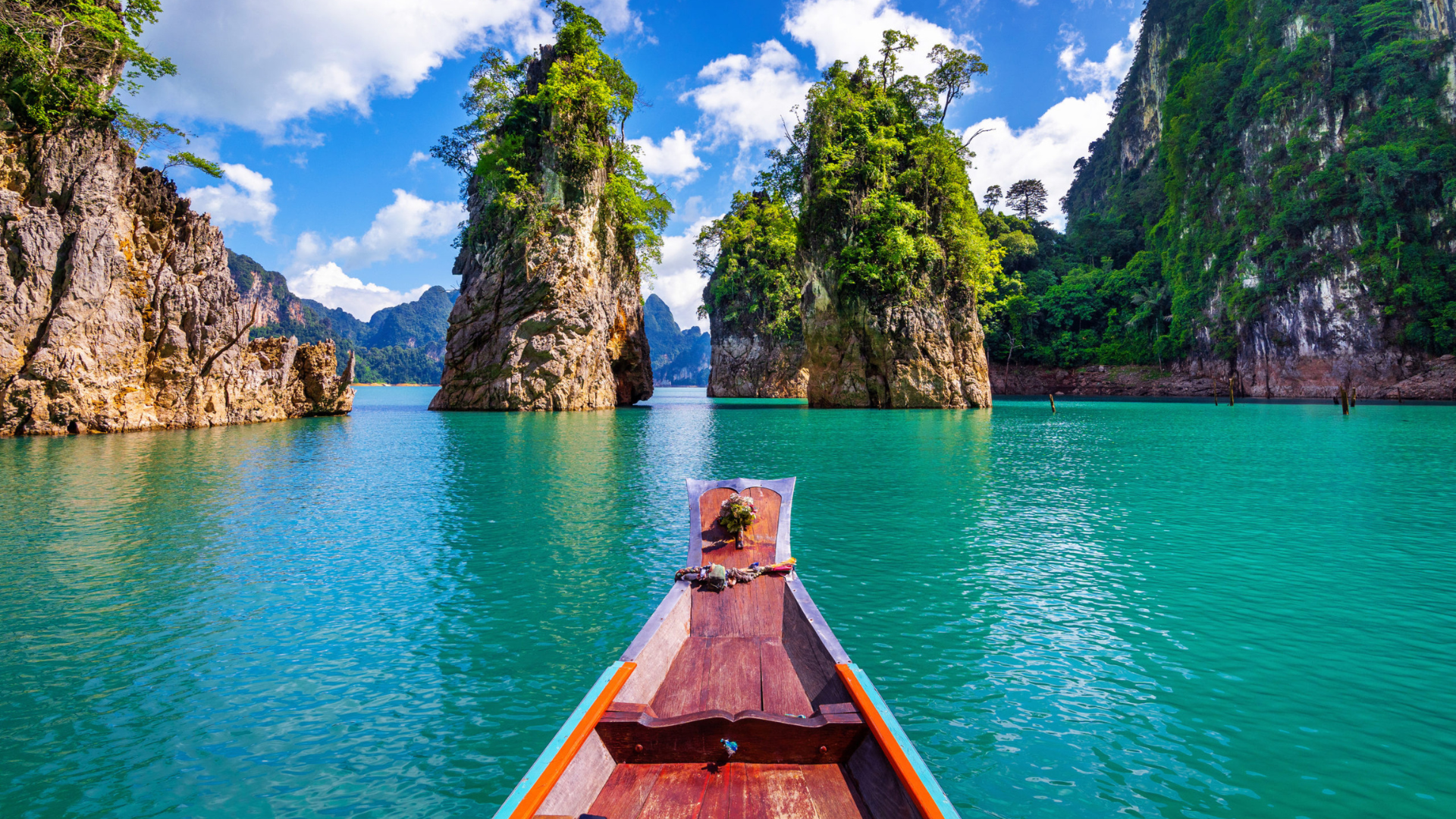 Bote de madera navegando en un lago de agua turquesa rodeado de formaciones rocosas y vegetación tropical.
