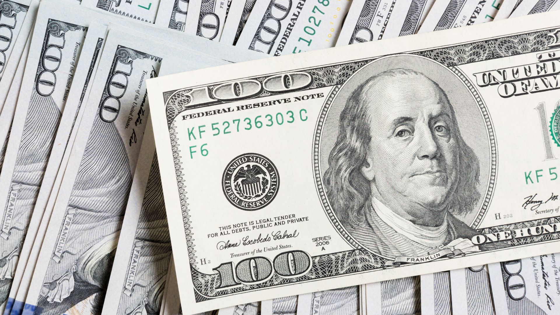 Billete de 100 dólares estadounidenses sobre varios fajos de la misma denominación.