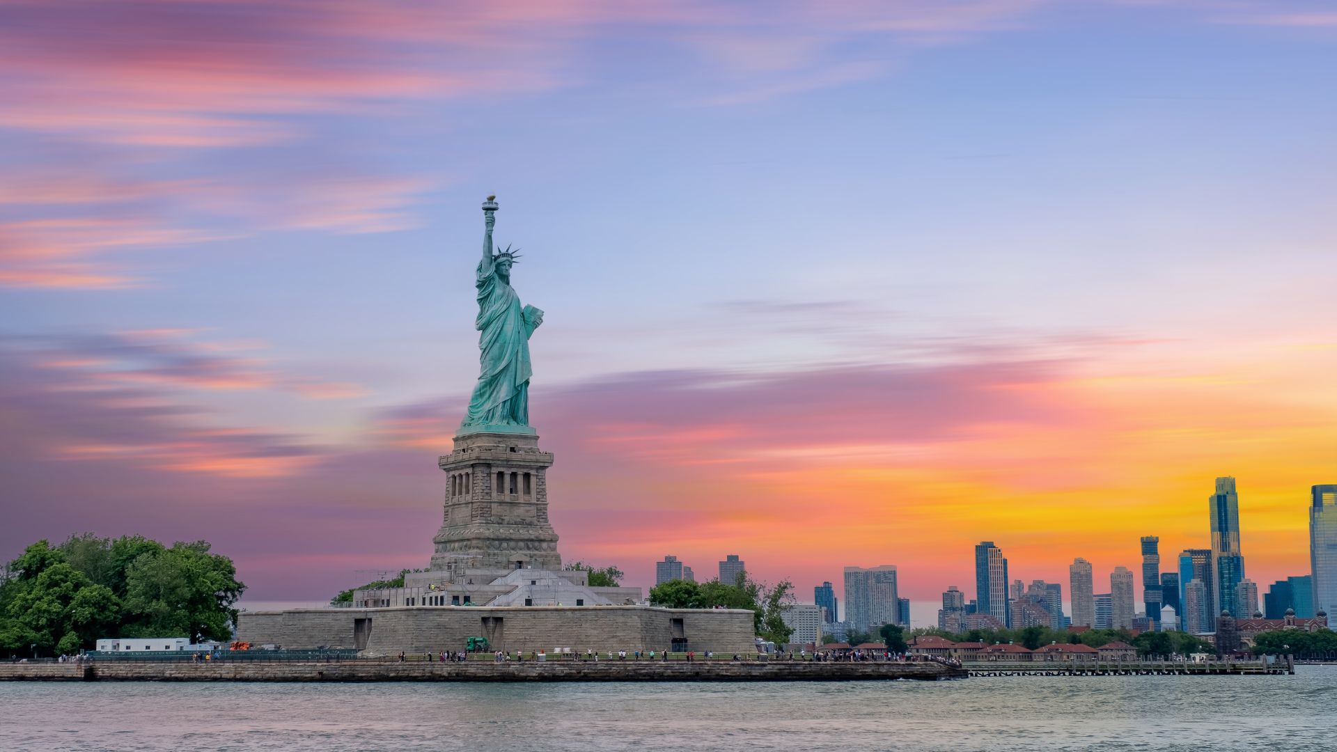 La Estatua de la Libertad al atardecer con el skyline de Nueva York al fondo.