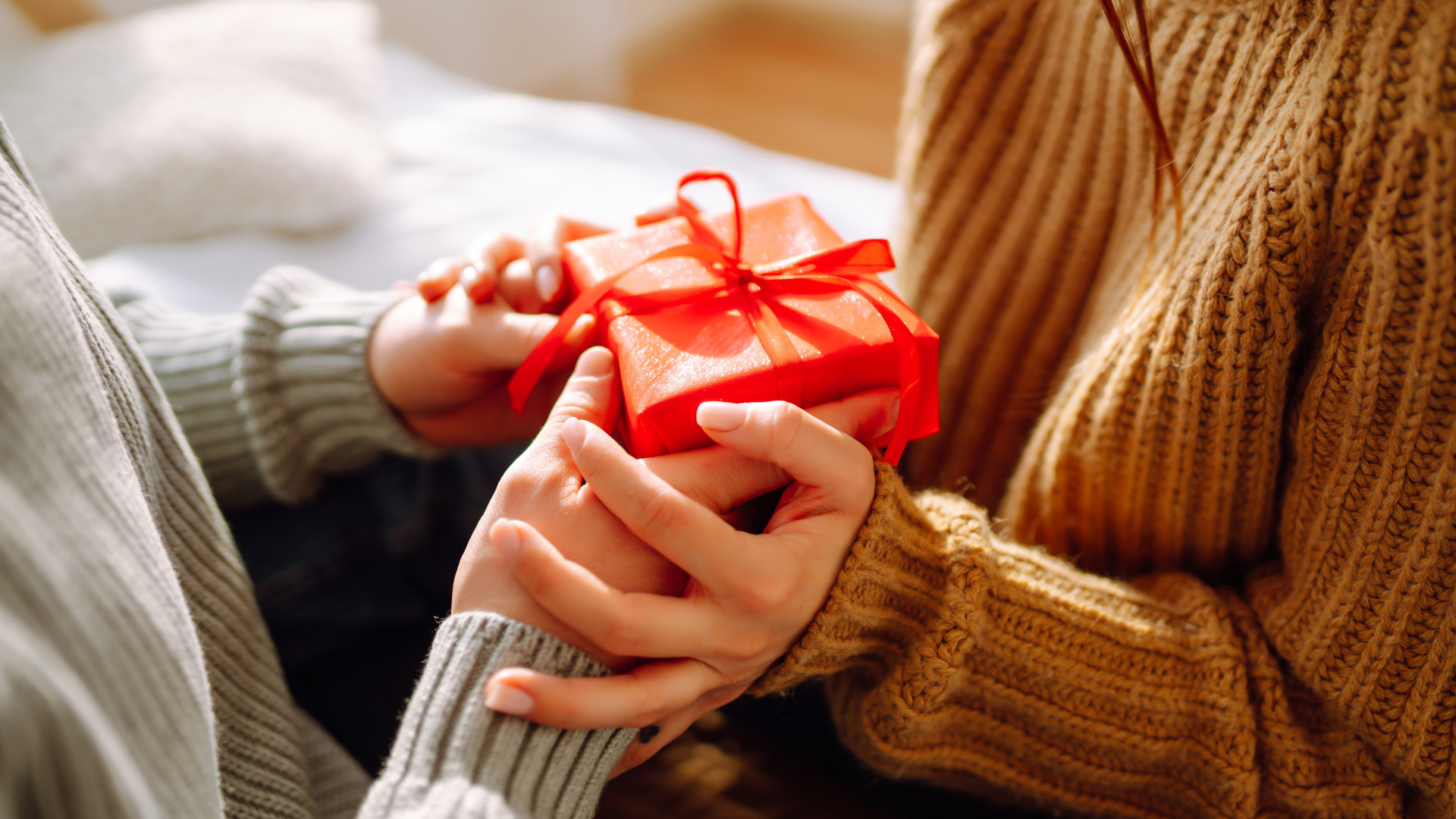 Persona entrega una pequeña caja de regalo roja con lazo a otra persona.