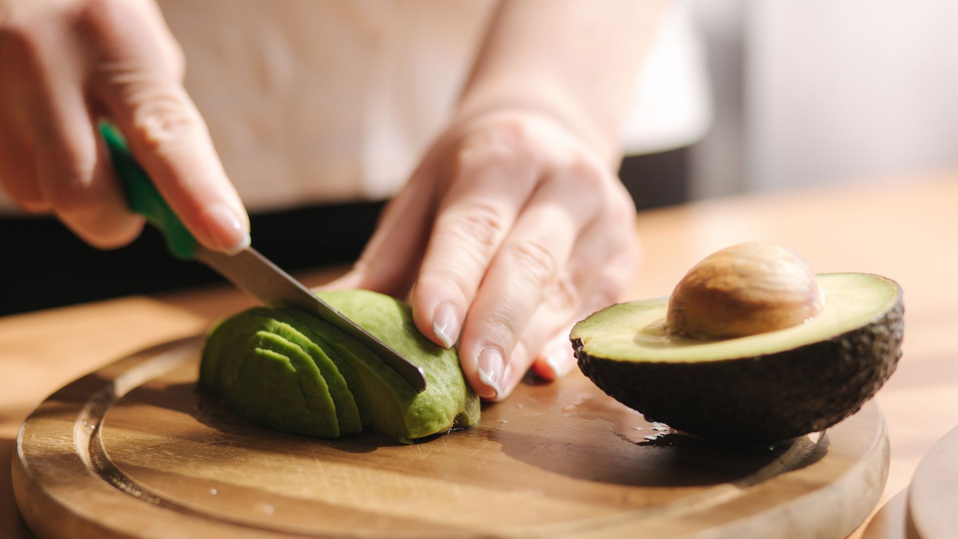 Persona cortando aguacate en rodajas sobre una tabla de cocina.