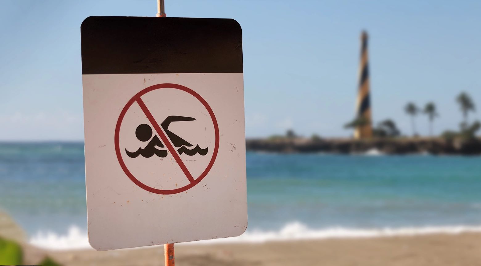 Señal de “prohibido nadar” en una playa, indicando restricción en el uso del balneario.