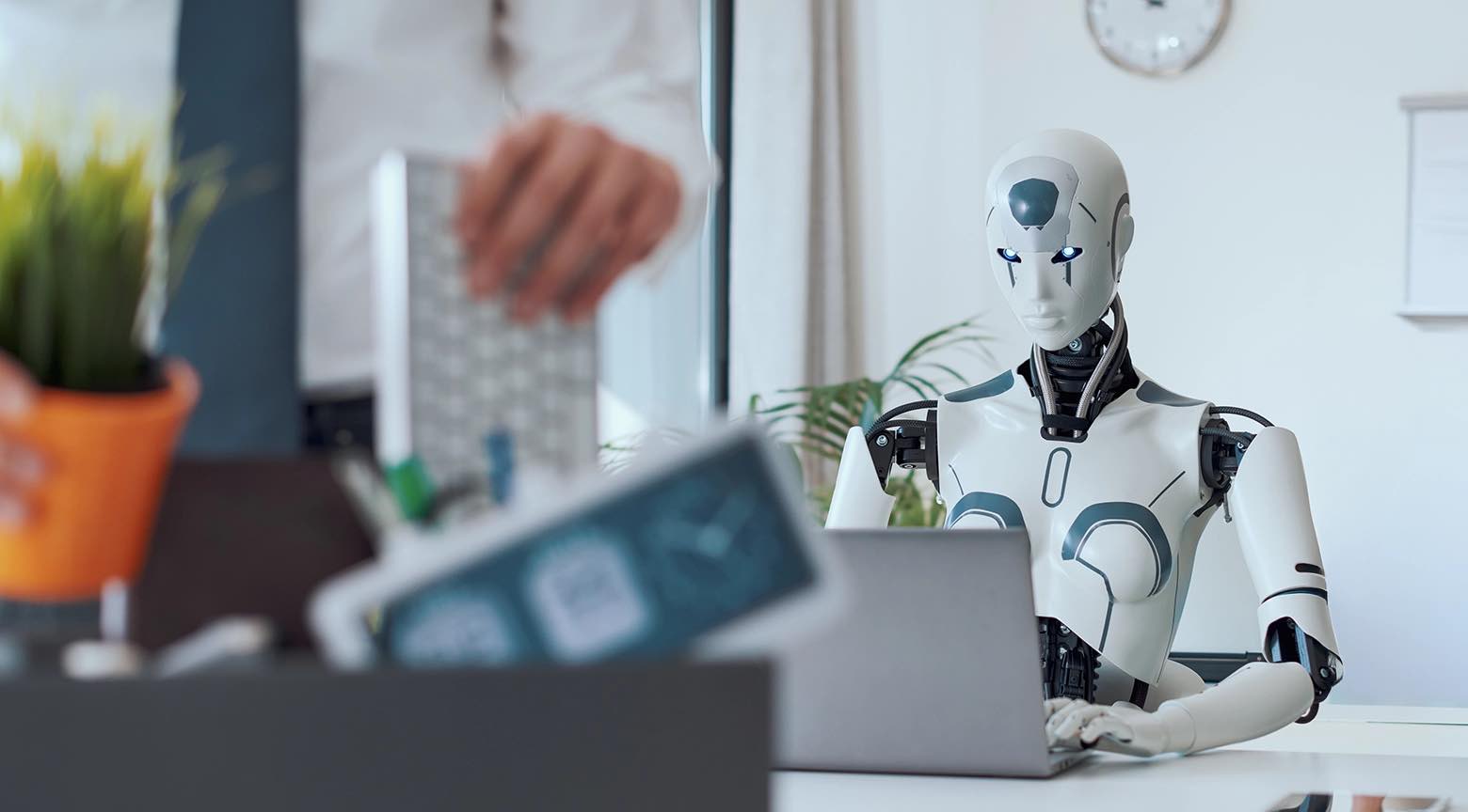 Robot humanoide trabajando en computadora mientras una persona paga con tarjeta en primer plano.