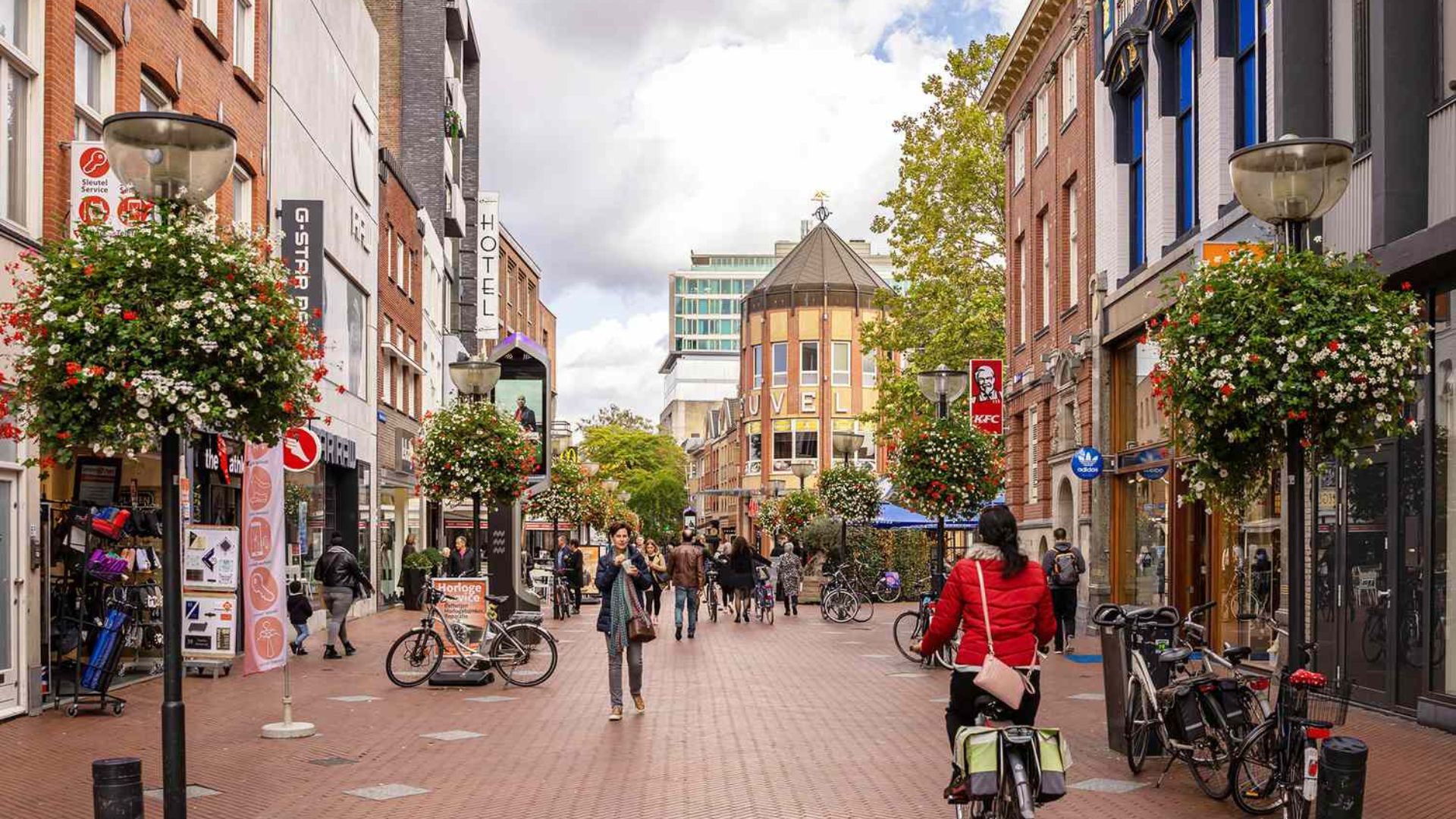 Personas caminando y montando bicicleta en una calle comercial peatonal de una ciudad europea.